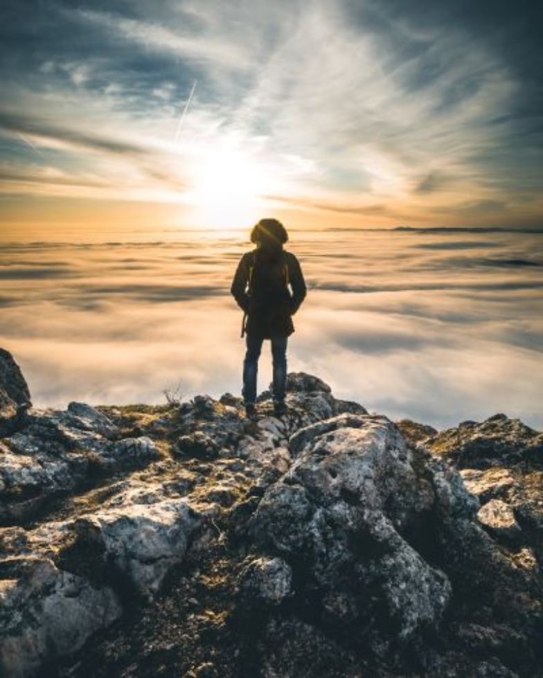Mann steht am Berg und Blick in den Sonnenuntergang