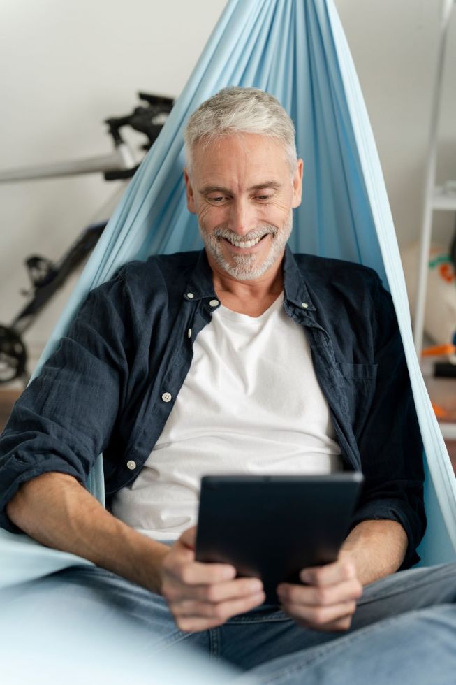 Lächelnder reifer Mann mit digitalem Tablet in der Hängematte