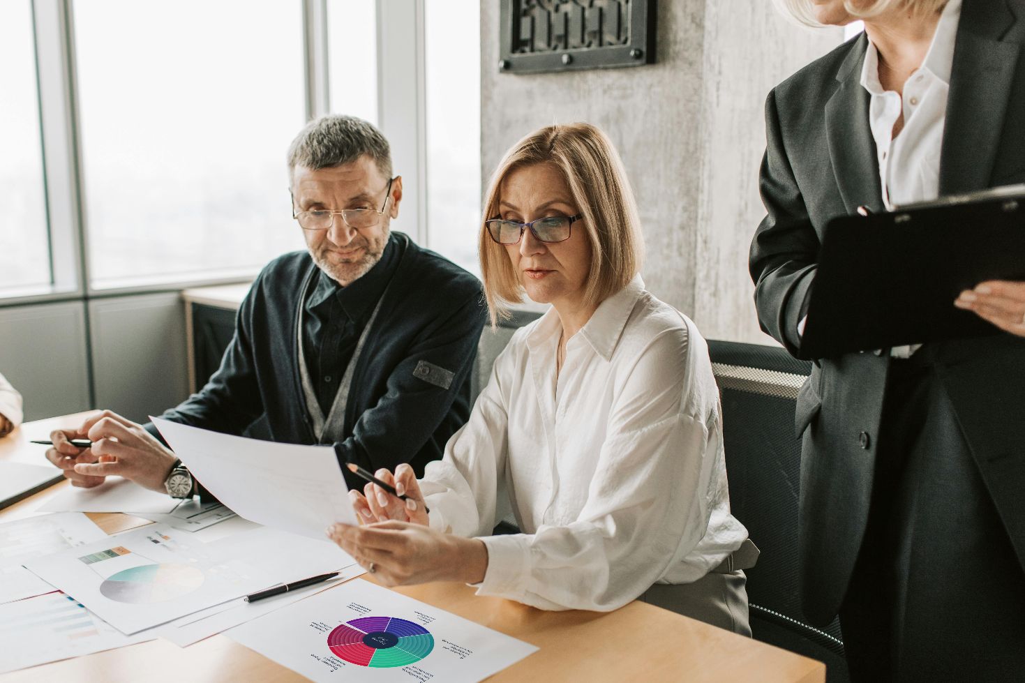 Drei Personen rund um einen Schreibtisch. Auf dem Schreibtisch Papiere auf denen eine DigComp Grafik abgebildet ist.