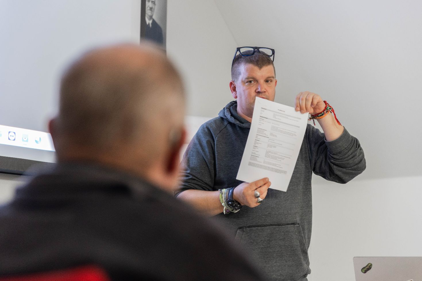 Mann steht in einem Raum und hält ein bedrucktes Blatt Papier in die Kamera