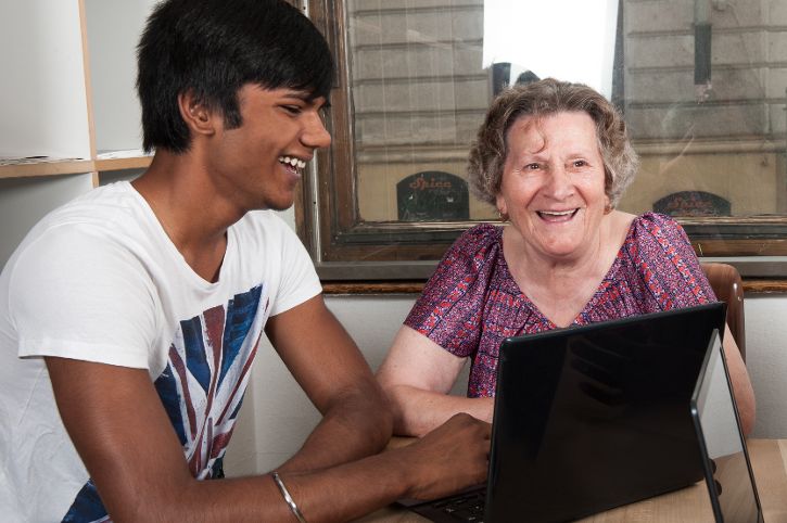 Das Bild zeigt einen jungen Mann und eine lächelnde ältere Dame die vor einem Laptop sitzen. © Fritz Harich - Qualitätszeit