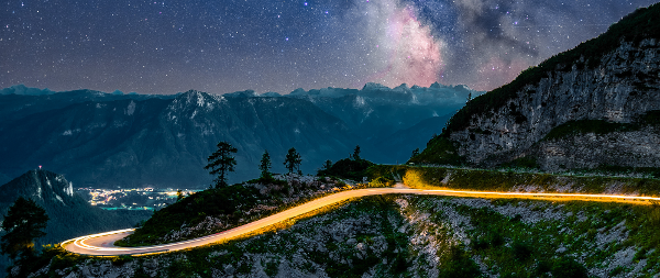 Berg mit Straße, auf der sich ein Lichtstrahl befindet unter einem Sternenhimmel © Samir  - AdobeStock 