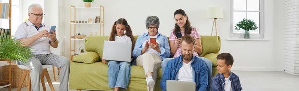 Große Familie, die zu Hause auf dem Sofa sitzt und verschiedene elektronische Geräte nutzt. Großeltern, Eltern und Kinder surfen im Internet, spielen Spiele oder unterhalten sich mit mobilen Apps.  &copy; Studio Romantic 