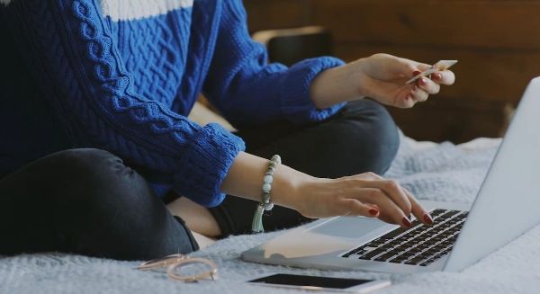 Frau sitzt vor dem Laptop und hat eine Bankomatkarte in der Hand.