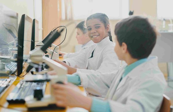 Drei Kinder, die in Laboruniform vor einem Computer und Mikroskop sitzen ©  Unsplash+ 