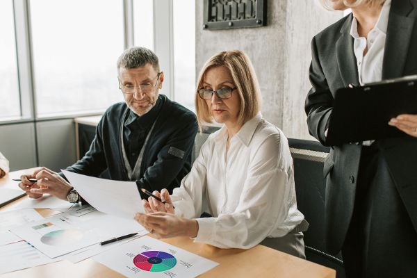 Drei Personen rund um einen Schreibtisch. Auf dem Schreibtisch Papiere auf denen eine DigComp Grafik abgebildet ist. &copy;  pexels 