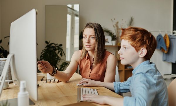 Frau sitz mit jungen Buben vor Computerbildschirm und scheint ihm etwas zu erklären.
