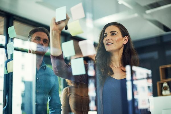 Frau vor Glasboard mit Haftnotizen stehend.