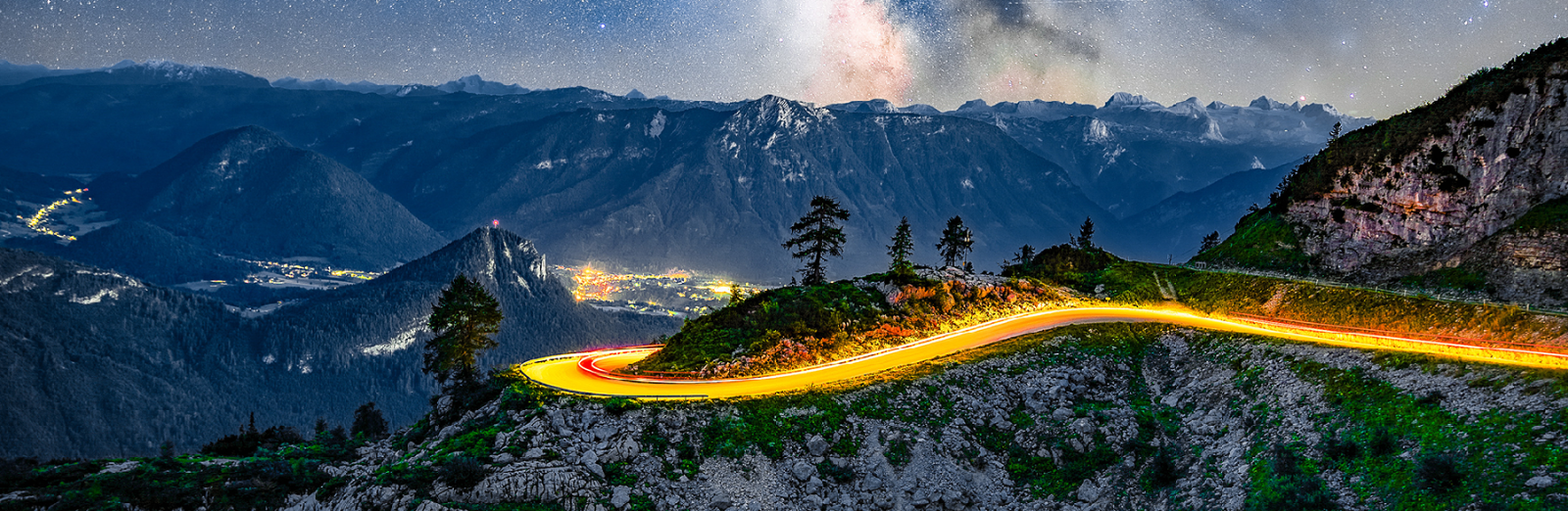 Berglandschaft im Dunkeln mit einen Leuchtspur auf der Serpentinenstrasse. Im Tal ist das Dorf erleuchtet. &copy; AdobeStock/Samir  - AdobeStock/Samir 