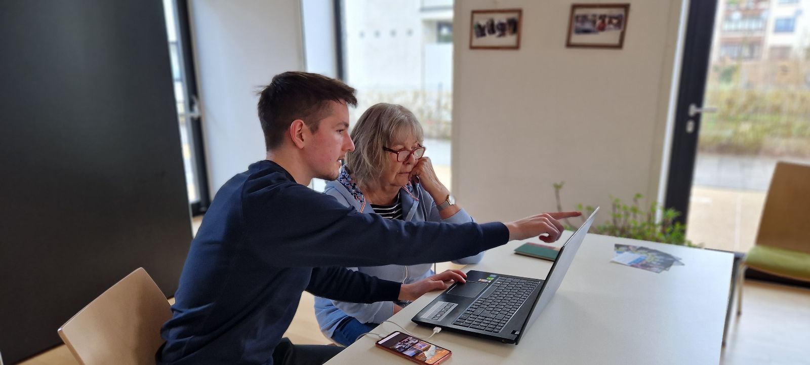 Ein junger Mann und eine ältere Frau sitzen in einem Büro vor einem Laptop, er erklärt ihr etwas. © Diakoniewerk - Diakoniewerk