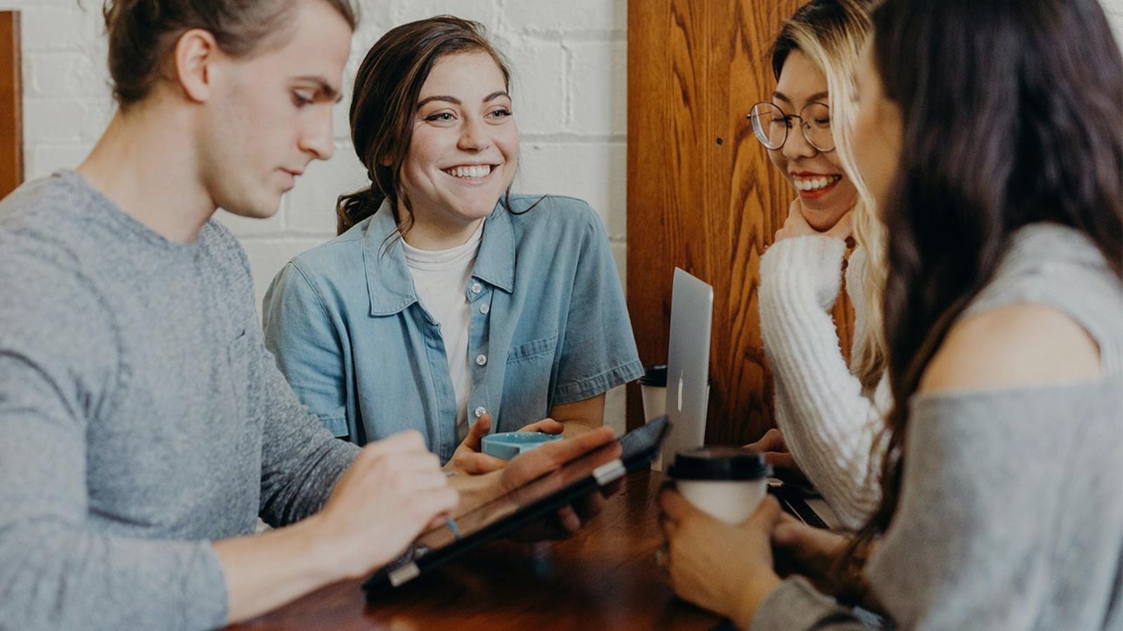 Gruppe von Personen steht an einem Tisch und unterhält sich, während eine Person ein Tablet in der Hand hält © Brooke Cagle - Unsplash