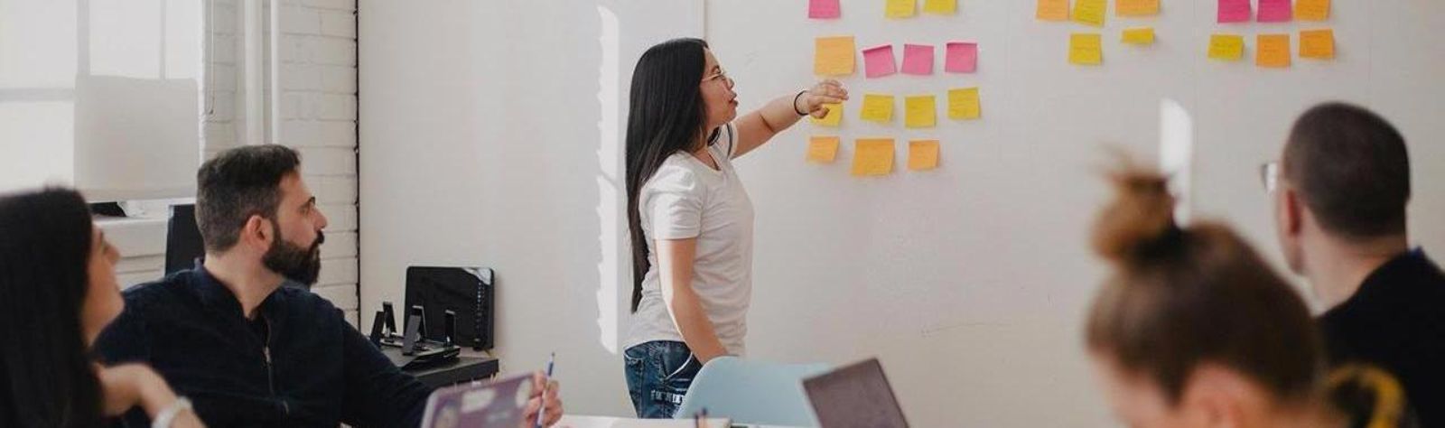 Frau steht vor einem Whiteboard und unterrichtet eine Gruppe von Personen © Jason Goodman - Unsplash