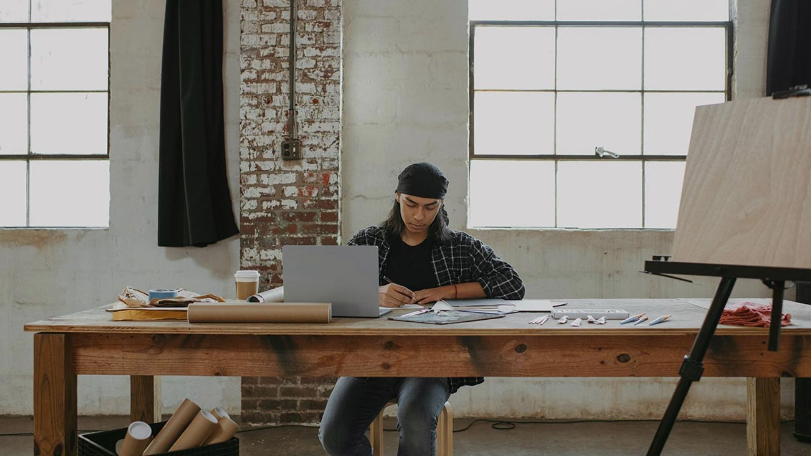 Mann sitzt auf einem Tisch mit Laptop und künstlerischem Werkzeug © Surface - Unsplash