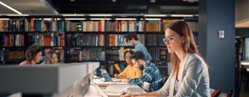 Universitätsbibliothek: Talentiertes kaukasisches Mädchen sitzt am Schreibtisch, benutzt Laptop, schreibt Notizen für die Hausarbeit, Aufsätze, lernt für die Klassenaufgabe. Vielfältige Gruppe von Studenten lernt, lernt für Prüfungen. © Gorodenkoff  - AdobeStock 