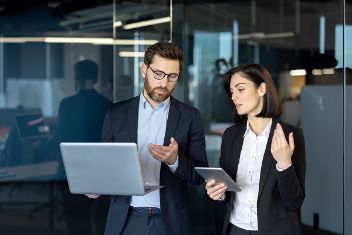 Frau und Mann in Businesskleidung halten Tablet und Laptop in den Händen © Liubomir  - AdobeStock 982128984 
