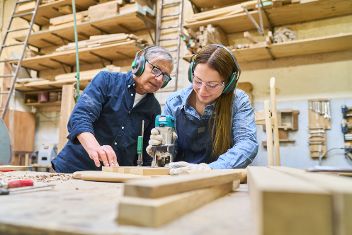 Junger Lehrling lernt unter Anleitung eines erfahrenen Mentors die Fertigkeiten der Holzbearbeitung. &copy; Robert Kneschke  - Adobe Stock 