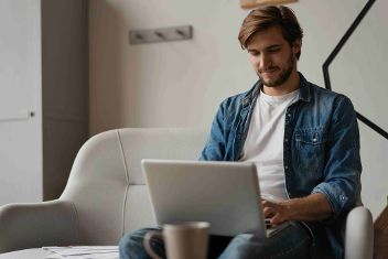 Mann sitzt lächelnd mit Laptop auf einer Couch ©  Unsplash+ 