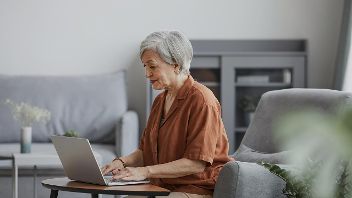 Seniorin sitzt lächelnd vor einem Laptop ©  Unsplash+ 