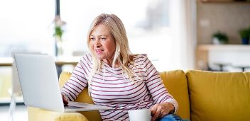 Ältere Frau sitzt mit Kaffeetasse vor Laptop ©  Unsplash+ 