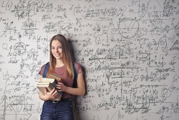 Mädchen mit Schulbüchern auf dem Arm an eine Wand gelehnt. &copy; Andrea Piacquadio  - Pexels 