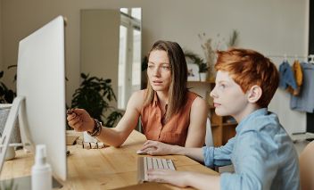 Frau sitz mit jungen Buben vor Computerbildschirm und scheint ihm etwas zu erklären. © Julia M. Cameron  - Pexels 
