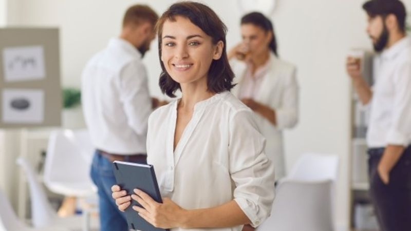 Glückliche erfolgreiche Geschäftsfrau oder Unternehmensleiterin, die im Büro steht, in die Kamera schaut und lächelt © 382881998 Studio Romantic  - AdobeStock_ 