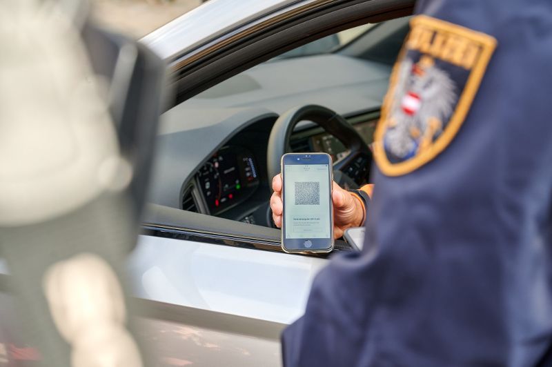 ein Smartphone mit dem QR Code des digitalen Führerscheins wird aus dem Auto heraus gezeigt. Der Exekutivbeamte - man sieht nur den Ärmel - wird überprüfen.