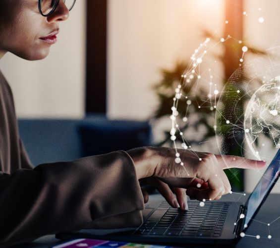 Woman sits in front of laptop. In the foreground you can see a hologram of the earth. The aim is to illustrate the interconnectedness of the world.