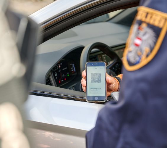 ein Smartphone mit dem QR Code des digitalen Führerscheins wird aus dem Auto heraus gezeigt. Der Exekutivbeamte - man sieht nur den Ärmel - wird überprüfen.