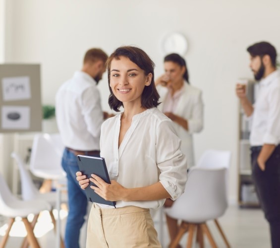 Glückliche erfolgreiche Geschäftsfrau oder Unternehmensleiterin, die im Büro steht, in die Kamera schaut und lächelt